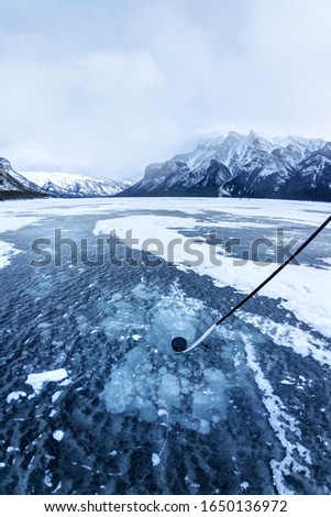 Playing ice hockey on frozen Lake Minnewanka in the Canadian Rockies of Banff National Park, Alberta, Canada. Hockey stick and puck with visible frozen methane gas bubbles under ice surface.