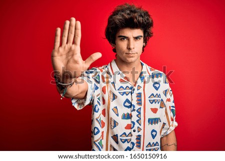 Young handsome man on vacation wearing summer shirt over isolated red background doing stop sing with palm of the hand. Warning expression with negative and serious gesture on the face.