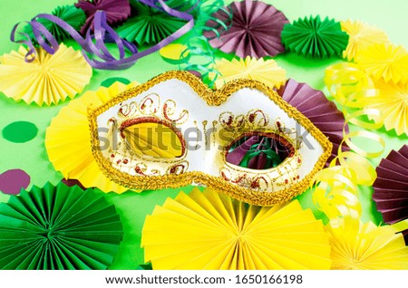 Colorful paper confetti, carnivale mask and colored serpentine on a green background with copy space, greeting card and party invitation template design for carnival or birthday, Mardi Gras,