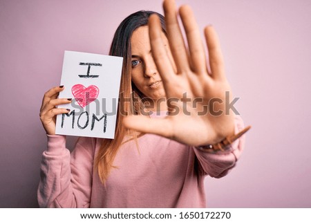 Young beautiful woman holding paper with love mom message celebrating mothers day with open hand doing stop sign with serious and confident expression, defense gesture