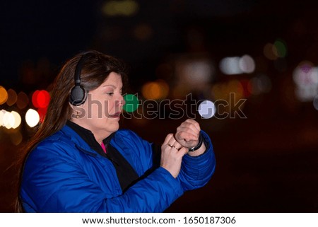 Lady interacts her smartphone, smartwatch and headphones when she is outside in the city at night.