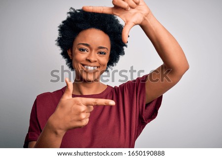 Young beautiful African American afro woman with curly hair wearing casual t-shirt standing smiling making frame with hands and fingers with happy face. Creativity and photography concept.
