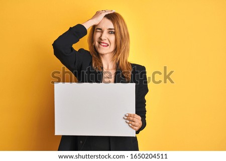Redhead business caucasian woman holding banner over yellow isolated background stressed with hand on head, shocked with shame and surprise face, angry and frustrated. Fear and upset for mistake.