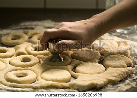 Woman making holes in raw homemade doughnuts pastry on the kitchen table, preparations for Fat Thursday holiday, european tradition before Easter Royalty-Free Stock Photo #1650206998