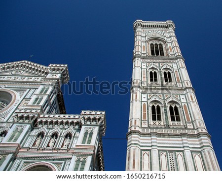The front facade and the tower of the Florence Cathedral, formally the Cattedrale di Santa Maria del Fiore, structurally completed by 1436 on a sunny summer day with a blue sky as background.
