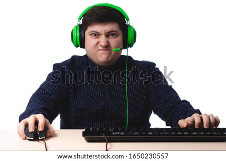 A young guy in a dark blue shirt green headphones gamer angry on a white background. isolate. copy space