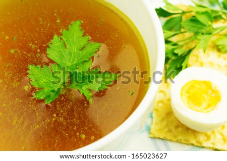 Bouillon, broth, clear soup in a white cup with a loaf, parsley, boiled egg on the tablecloth. Close-up.