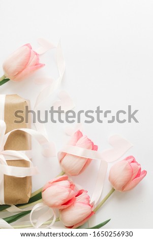 Pink tulips flat lay with ribbon and gift box on white background, space for text. Stylish vertical image. Happy womens day. Greeting card mockup. Happy Mothers day. Hello spring
