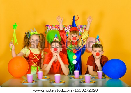 Four children with a clown at the festive table, raise their hands up