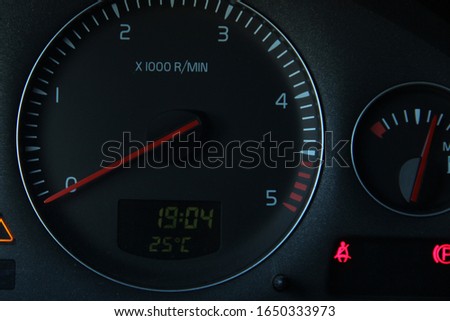Black car dashboard with a view of the speedometer. Illuminated red belt and parking symbols. Orange backlit warning sign.