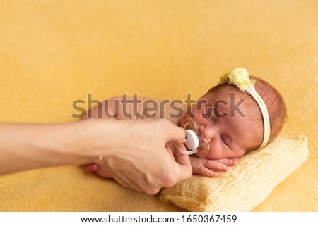 babyhood, motherhood and people concept - mother's hand giving pacifier to little baby daughter lying on knitted yellow blanket of knitted pillow