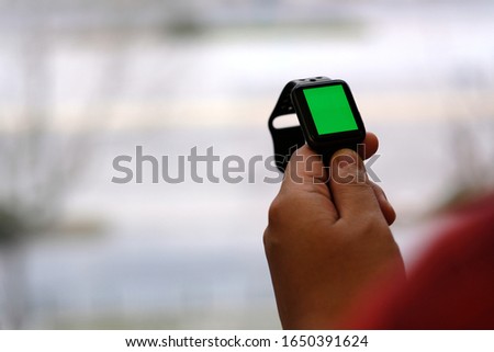 over shoulder of one person holding green screen smart watch. blur background