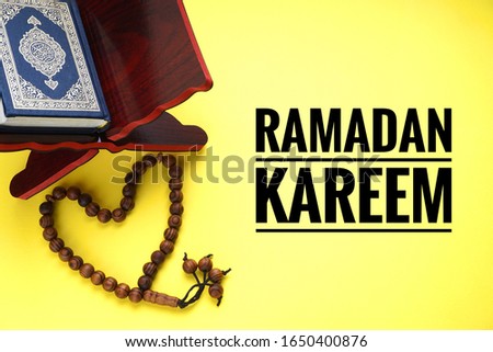 RAMADAN KAREEM text and Holy Al Quran book written with arabic calligraphy and its meaning of Al Quran with tasbih, misbaha or Muslim rosary beads on yellow background. Copy Space             