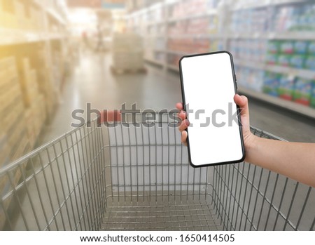Mobile smartphone with a white screen with a background in the supermarket and the copying area. People are showing mobile phones above the cart.