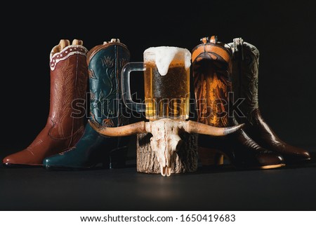 Western Wear Boots, Cow Skull, Pitcher of Beer on Dark Background Royalty-Free Stock Photo #1650419683