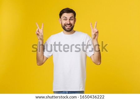 Young handsome man wearing striped t-shirt over isolated yellow background smiling looking to the camera showing fingers doing victory sign. Number two