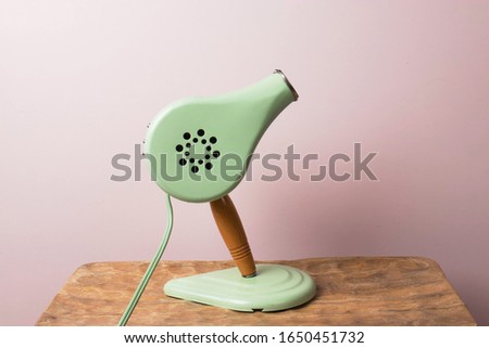 Cute vintage blow dryer on rose colour background. Styling tool from the 1950's or 1960's. Heat blower for drying and styling. Minimal concept with muted colours. Self care grooming tools. Copy space.