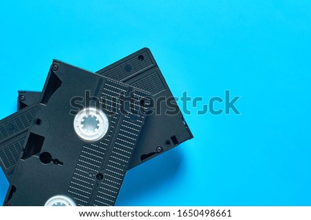 Heap of three black old vhs video cassettes lies on blue desk. Concept of 90s. Copy space. Top view