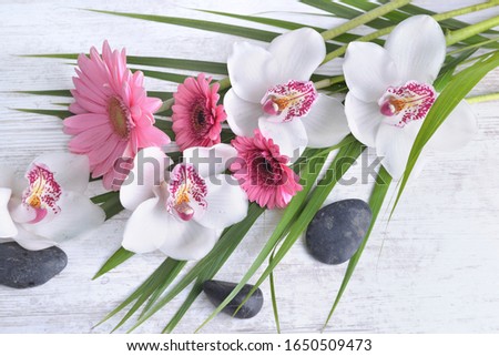 beautiful bouquet of white orchids and pink daisies in leaf and pebbles on white table background 