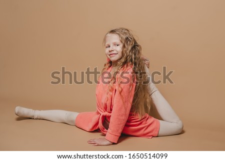 Little girl in red bathrobe is doing stretching. Child active positive cheerful smile workout. Brown background place for text.