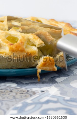 Bramley apple pie with lattice pastry topping being sliced with a cake cutter on a blue plate. Blue tile background