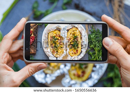 Woman take picture of food with phone. Smartphone lunch photo of baked stuffed potato in the kitchen. Vegan healthy diet food. Lifestyle trendy social media style.