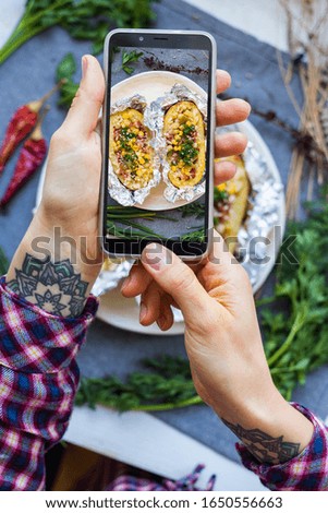 Woman take picture of food with phone. Smartphone lunch photo of baked stuffed potato in the kitchen. Vegan healthy diet food. Lifestyle trendy social media style.