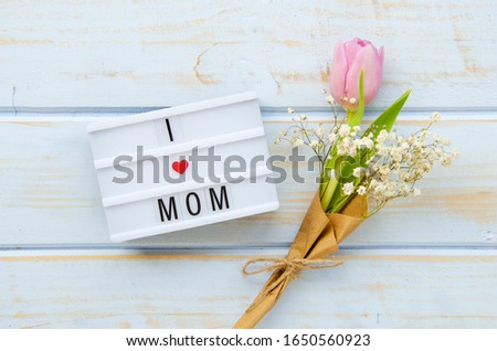 Top view lightbox with a sign I love my mom with red heart and bouquet with one tulip on a wooden background. Mother's day, 8 march concept