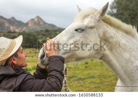 white horse in the green meadow receiving cuddles from his cowgirl with the white cowboy hat with many hugs and caresses and kisses