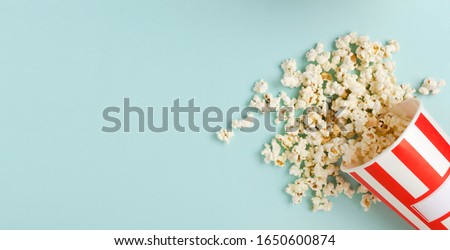 Top view of fresh spilled popcorn from the striped paper bowl on the bright blue background.Empty space for design