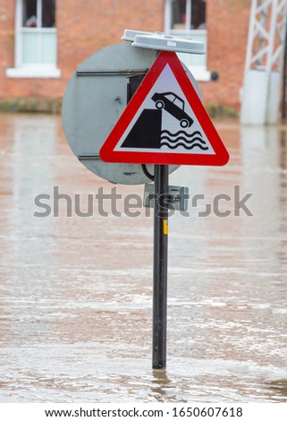 Partly submerged Danger of Quayside or River Bank sign due to the road being flooded by The River Ouse in York, England.