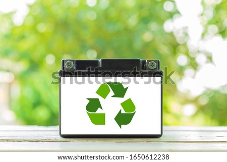 Black old battery with recycle icon on white wooden table with nature background.