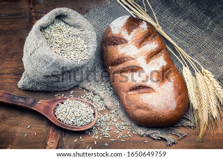Rye bread with grain in a wooden spoon lies on a wooden rustic table. The bread lies on a coarse sackcloth with ears of wheat. Copy space. View top. Focus concept.