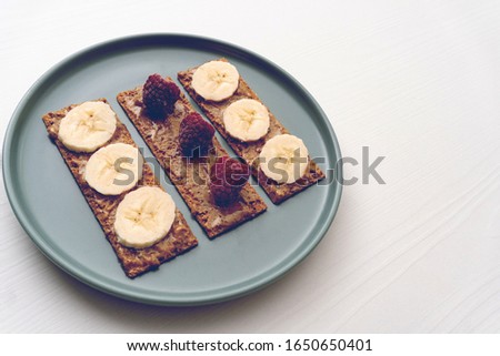 Peanut butter, raspberry and banana on bread slices on round plane on white table, toast for morning breakfast or snack for brunch, minimal concept, healthy eating, toned
