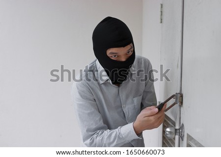 Masked thief in black balaclava trying to break into house