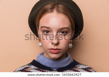 Photo of pretty calm woman in earrings posing and looking at camera isolated over beige background