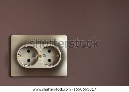 Golden double power socket on a painted brown wall. Standard european electrical connector close-up