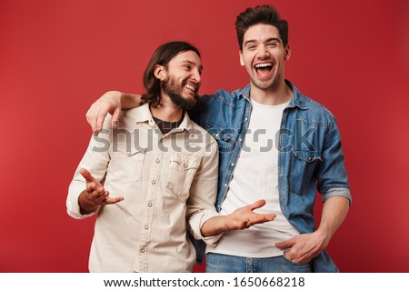 Two cheerful young men wearing casual clothes standing isolated over red background, laughing Royalty-Free Stock Photo #1650668218