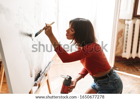 Portrait of young caucasian artistic woman using painting tools while drawing picture in studio
