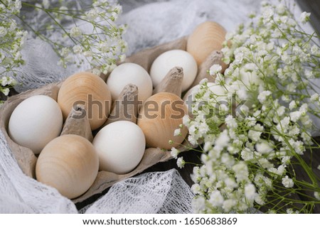Happy Easter. White chicken eggs, wooden eggs in a stand on a wooden background with white gypsophila flowers. The concept of holidays. Trend.