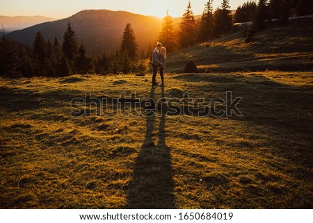 Warm evening sun light. Happy young couple hugging and kissing at sunset with amazing mountain view and pine forest. Silhouette.