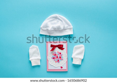 Top view of greeting card and baby hat and mittens on blue background, concept of mothers day