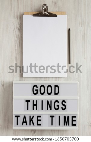 'Good things take time' words on a modern board, clipboard with blank sheet of paper on a white wooden background, top view. Overhead, from above, flat lay.