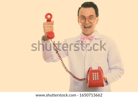 Studio shot of happy crazy man doctor smiling while giving old telephone