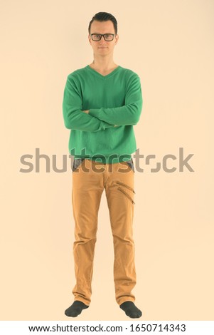 Full body shot of young handsome man wearing eyeglasses with arms crossed