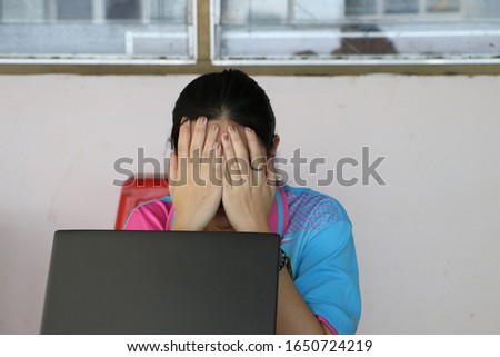 a student is  hiding face laughing timid with her laptop on white wall background. they wear a ring on left hand. 