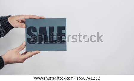 Close Up Of Man Hands Holding A Sign Saying "Sale" On White Background. Advertising Space. Board For Sale. High Quality Photo
