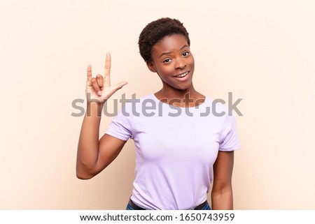 young pretty black womanfeeling happy, fun, confident, positive and rebellious, making rock or heavy metal sign with hand