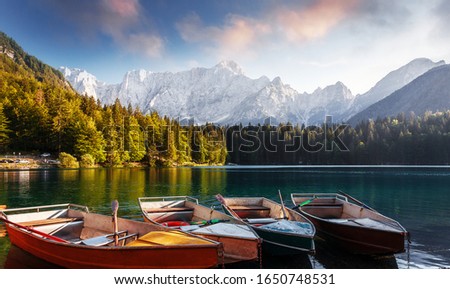 Beautiful view on Fusine lake side. Scenic image of fairy-tale lake with boats on water and colorful sky. Wonderful Autumn scenery. Amazing nature Background. Awesome dramatic scene. Julian Alps