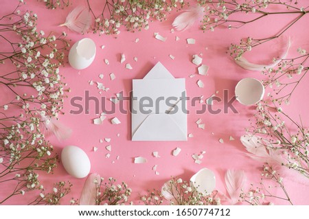 Blank greeting card, kraft envelope. Easter eggs and gypsophila flowers on a pink background. Flat lay, top view.